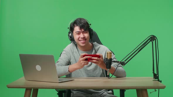 Man With Headphone Looking At Camera While Using Mobile Phone Playing Game On Green Screen