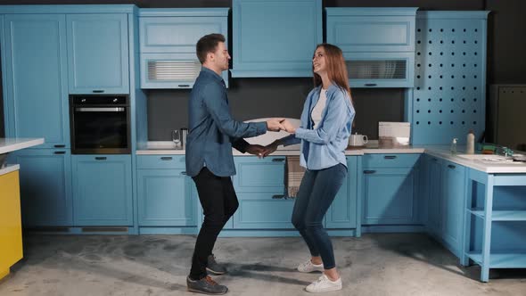 Happy Young Couple Fun Dancing While Cooking in the Kitchen at Home. They Holding Their Hands