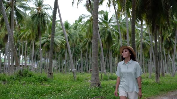 Slow motion of a young woman with hat looking at coconut trees in the garden