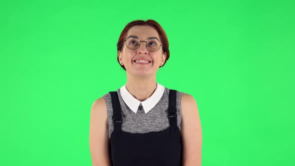 Portrait of Funny Girl in Round Glasses Is Daydreaming and Smiling Looking Up. Green Screen