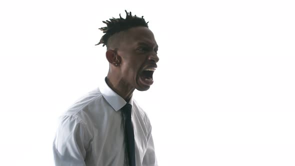 Black man in office clothes stands on white background and shouts indignantly, side view