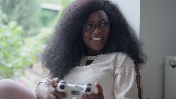 Happy Female Gamer Playing Online with Game Controller Smiling Looking Away Sitting on Windowsill