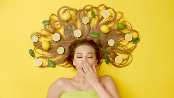girl on colored background with citrus fruits on long hair and yawns,young woman awakening morning 