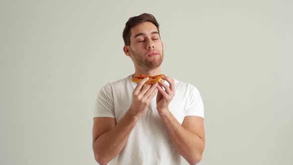 Studio Portrait of Hangry Young Man Biting Into Slice of Pizza Smelling Tainted Unappetizing Food