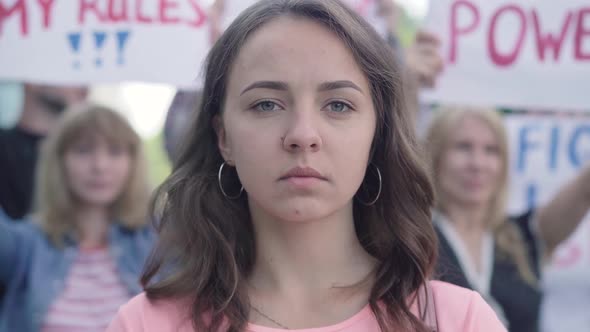 Close-up Portrait of Young Beautiful Woman Closing Mouth with Hands As Crowd of People Protesting at