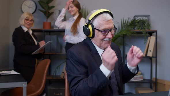 Joyful Senior Businessman Working on Portable Laptop Sitting at Desk Listening Music and Dancing