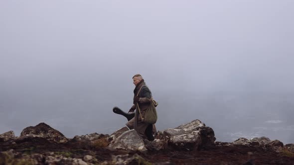 Travelling Man Carrying Guitar Case And Walking Over Misty Rocks