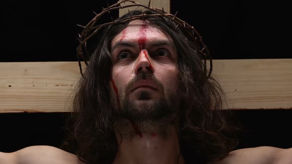 Frightened Jesus Christ With Bleeding Body Crucified on Cross Looking at Camera