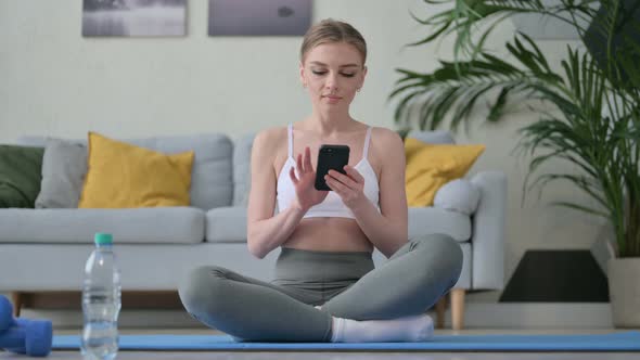 Young Woman Using Smartphone on Yoga Mat at Home