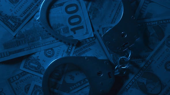 Close Up of Rotation Metal Handcuffs Over Stack of Dollar Banknotes
