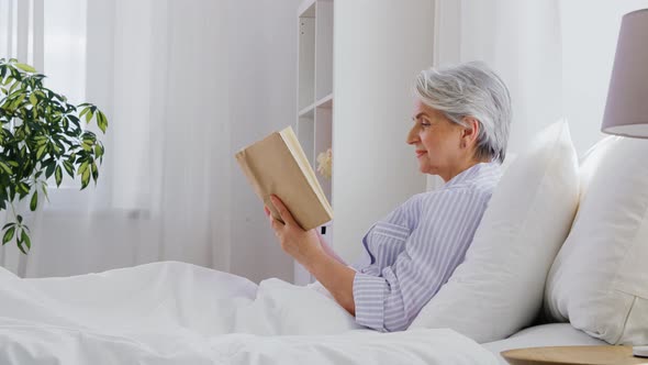 Senior Woman Reading Book in Bed at Home Bedroom