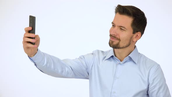 A Young Handsome Man Takes Selfies with a Smartphone - White Screen Studio