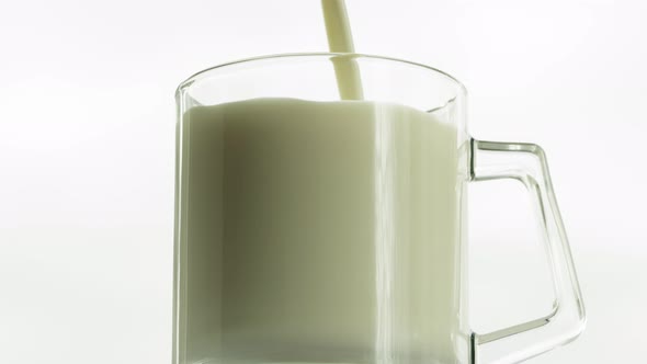 Milk is Poured Into a Transparent Glass Cup That Rotates on a White Background Closeup