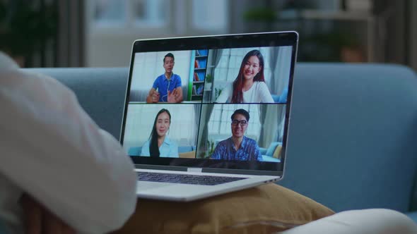 Man Greeting With Colleagues In Video Conference Call From Laptop While Lying On Sofa