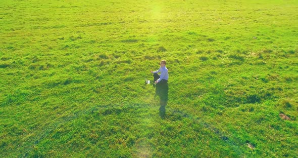 Low Orbital Flight Around Man on Green Grass with Notebook Pad at Yellow Rural Field