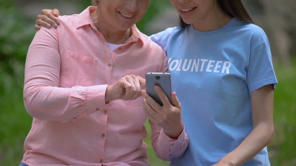 Happy Aged Woman Showing Smartphone Photos to Young Volunteer, Communication