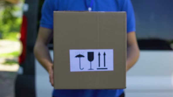 Courier in Uniform Holds Box With Keep Dry, Fragile, This Way Up Signs, Service