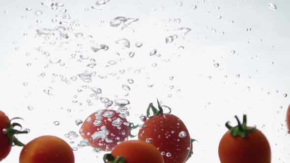 Closeup of Fresh and Health Cherry Tomatoes Falling Into Clear Water with Big Splash on White