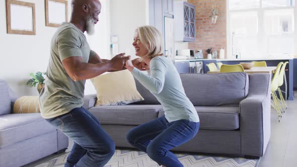 Mixed race senior couple dancing together in the living room at home