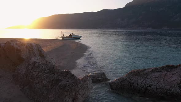 View of Wild Beach with Calm Sea Waves Boat and Mountains at Sunset