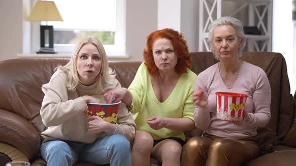 TV POV of Three Absorbed Caucasian Adult Women Watching Movie Eating Popcorn Sitting on Couch at