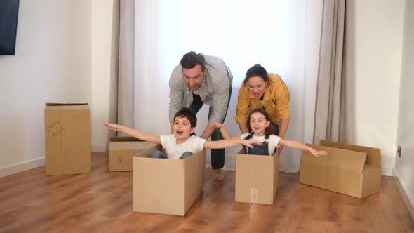 Multiracial Family of Four Have Fun in New House Parents Riding Kids in Cardboard Boxes