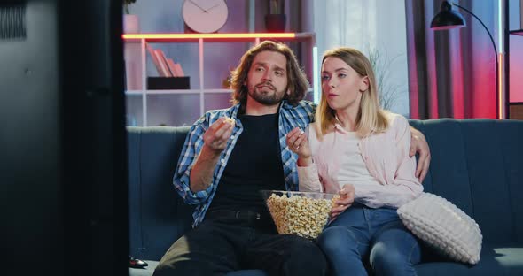 Couple Sitting on the Couch in Front of TV, Eating Popcorn, Talking