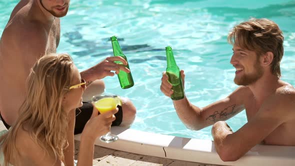 Two Smiling Caucasian Males in Pool Drinkin Beer with Blonde Female with Cocktail on Lounge