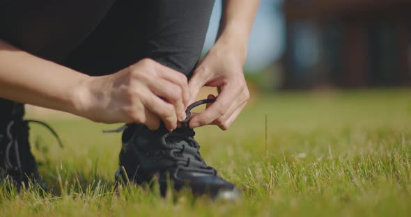 Close Up of Sporty Woman Crouching Outdoors in Sportswear and Tying Shoelace