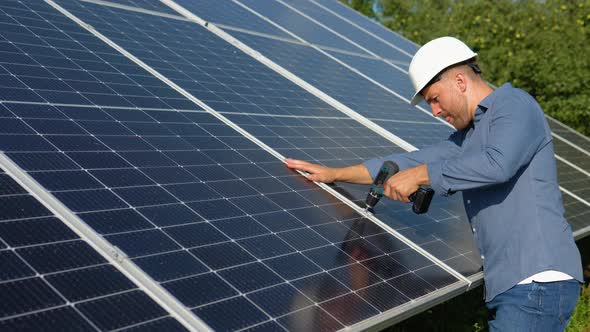 Male Engineer in Protective Helmet Installing Solar Photovoltaic Panel System Using Screwdriver