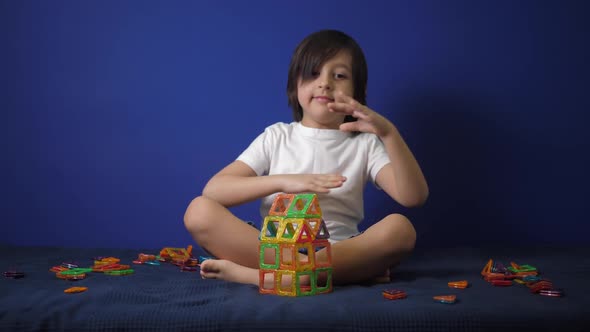 Boy Child in a White Tshirt is Sitting on a Bed Against a Blue Wall and Playing