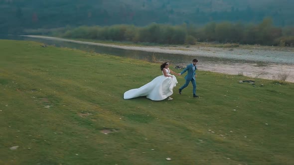 Wedding Couple Running Near Mountain River. Groom and Bride. Arial View