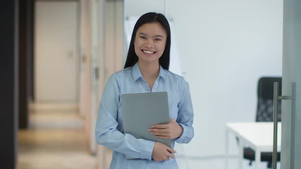 Young Positive Asian Woman Manager Carrying Laptop and Laughing to Camera Standing at Office