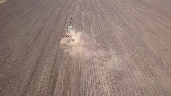 Top down aerial view of green tractor cultivating ground and seeding a dry field. 