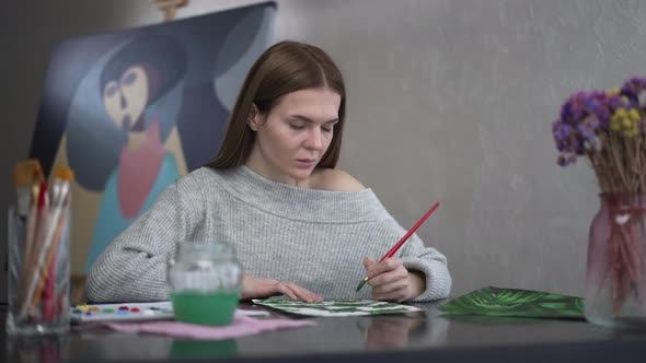 Portrait of Beautiful Woman Thinking Painting with Acrylic Colors on Paper Sitting at Table Indoors