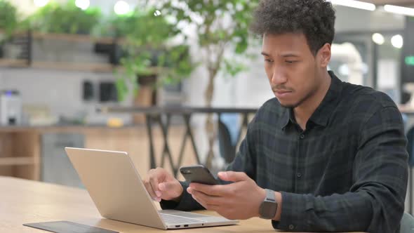 African American Man with Laptop Using Smartphone at Work