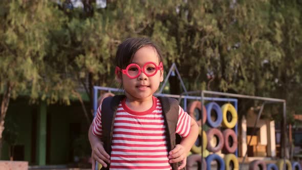 Cute smiling schoolgirl in summer clothes with a backpack standing at school.