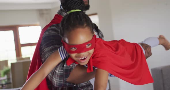 Happy african american father and daughter having fun, wearing superhero costumes