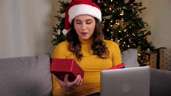 Woman in Santa Claus Hat Opens Gift Box and Surprised Online Video Call Laptop