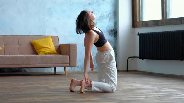 Cute Brunette Woman Does Yoga Exercises at Modern Home at Sofa Background