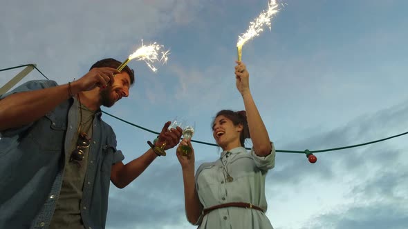 Low angle view of couple holding firework candles and toasting with champagne