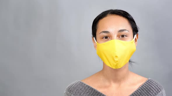 Young Smiling Mixedrace Woman with Yellow Medical Mask Against Gray Background