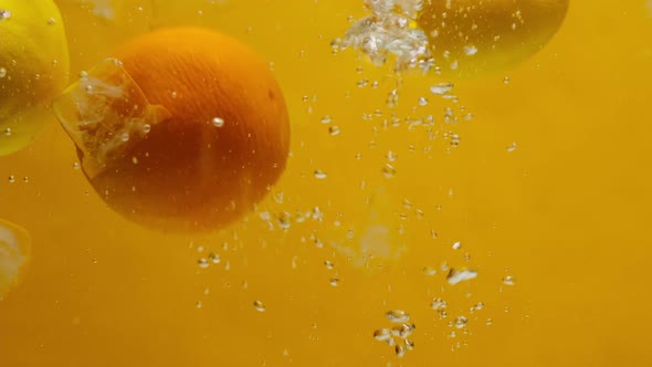 Closeup of Falling Limes Oranges and Lemons Into the Water on Orange Background Making a Cocktail of