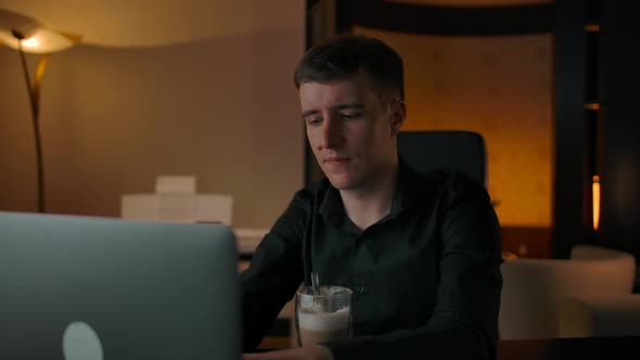 Interested Man Drinks Coffee at Home Looking at His Laptop in Living Room