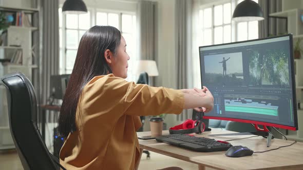 Asian Female Video Editor Stretching While Works With Footage And Sound On Her Personal Computer