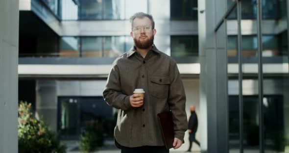 A Bearded Man Standing in the Courtyard of Office Center and Looking at Camera