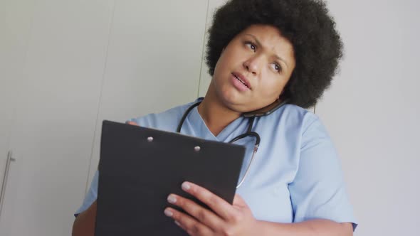 Video of focused plus size african american female doctor using smartphone and tablet