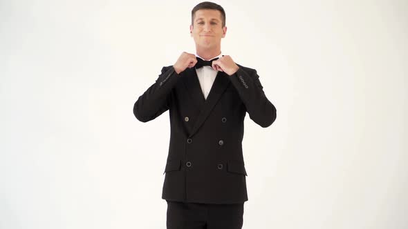 handsome man in a suit with bow tie is posing in front of a mirror at the exit of the room.