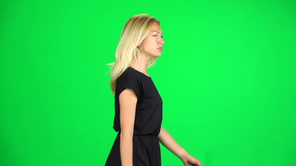 Pensive Woman Is Walking on a Green Screen at Studio. Slow Motion. Side View