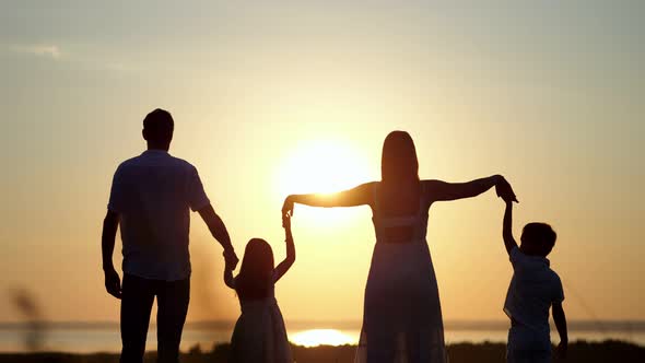 Family Looks at Sunset Raising Hands to Sky on Meadow